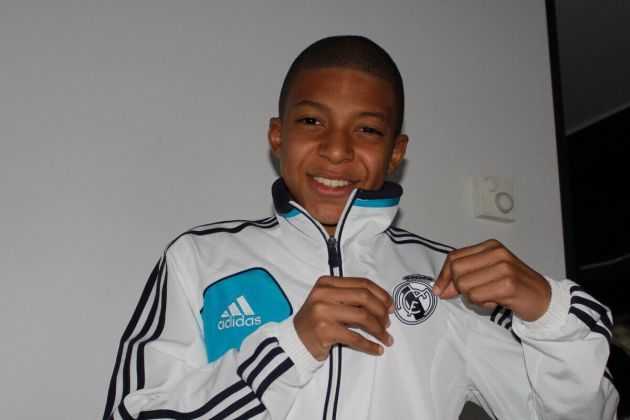 A young Kylian Mbappe pictured holding the Real Madrid crest on a club tracksuit.