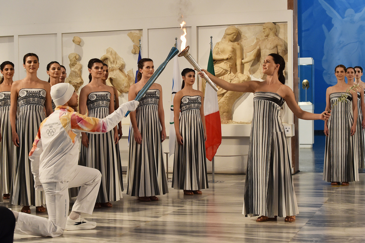 OLYMPIA, GREECE - NOVEMBER 26: High Priestess Mary Mina hands over the Olympic Flame to torchbearer Petros Gaidatzis during the lighting ceremony of the Olympic Flame for the Milano Cortina 2026 Olympic Winter Games on November 26, 2025 in Olympia, Greece. (Photo by Milos Bicanski/Getty Images)